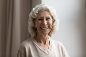 Fototapeta na wymiar Head shot portrait smiling mature woman with grey curly hair standing at home, beautiful overjoyed middle aged senior female looking at camera, feeling positive, posing for photo, happy retirement