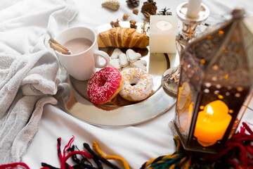Still life with delicious Christmas gingerbread and cookies  breakfast on a tray in bed , donuts and croissants , cup of cacao or latte with cinnamon, ginger biscuits figure, Christmas candles.