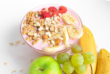 Yogurt with muesli and raspberries. Oatmeal, banana, nuts, apple, grapes on a white table close-up top view. The concept of healthy food, diet, healthy breakfast.