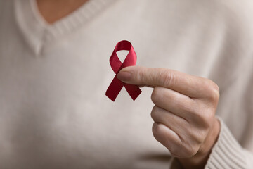 Close up mature woman holding red awareness ribbon in hand, middle aged female supporting people with disease, regular checkup promotion, symbol of fight against AID, HIV, cancer, drugs addiction