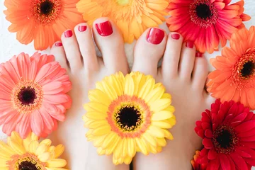 Fotobehang Toenails after pedicure with red nail varnish between flowers © Kzenon