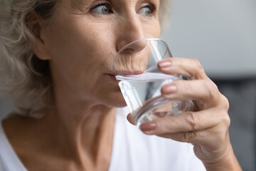 Close up thirsty beautiful middle aged woman drinking fresh pure mineral water, satisfied senior...