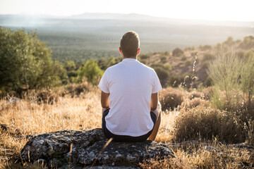 Naklejka na ściany i meble Persona sentada en una piedra en el campo mirando al horizonte y disfrutando de la naturaleza. 