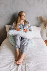 Fototapeta premium Pregnant girl sitting on bed in pajamas