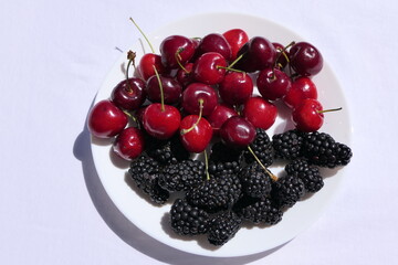 A white plate with dark ripe cherries and blackberries as dessert or snack