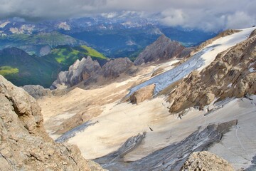 View from Marmolada summit. Sharp rocks with glacier, green meadows in the background. Clouds. Dolomites Mountains. 