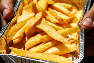 French fries in aluminium foil tray. Yummy potato fry close up. Fast food o street food takeaway service concept.