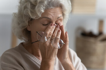 Close up exhausted mature woman suffering from eye strain, holding glasses, touching massaging nose...