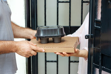Food delivery service man with pizza cardboard and take away coffee cups delivering food to customer at doorway. Food order and delivery service.