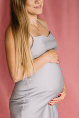 Pregnant girl model in gray dress on pink background