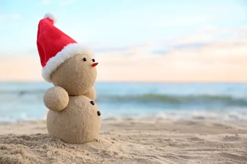 Snowman made of sand with Santa hat on beach near sea, space for text. Christmas vacation © New Africa