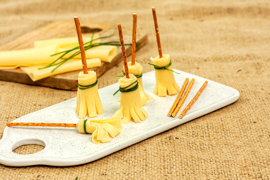 Halloween party food idea: broomstiks edible made of cheese, salty sticks and chives on the white plate.