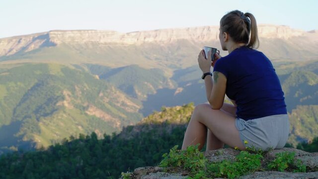 At the top of the mountain. Girl sits on a stone and drinks tea. The concept of tourism and recreation in the mountains
