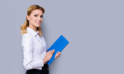 Happy smiling businesswoman holding blue folder, with copy space area for some slogan or text. Confident blond woman in white shirt, isolated over grey color background. Success in business concept.