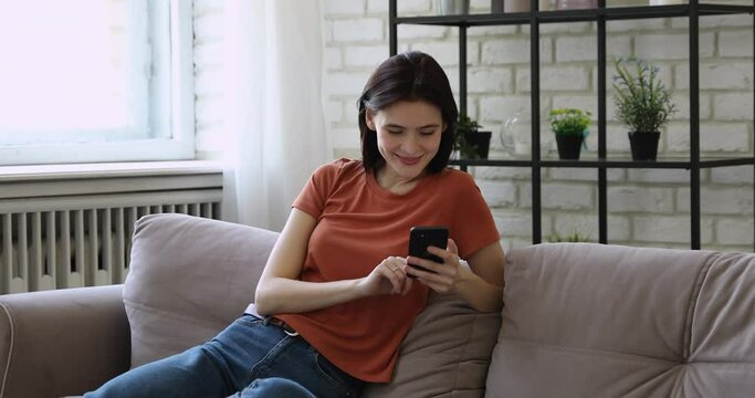 25s woman relax on couch in living room holds smartphone scrolling social media feed watch stories, share photos with friends waste free time, spend weekend using internet network chat on-line concept
