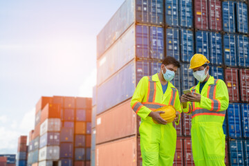 Engineer or worker man using a smartphone wearing mask and safety yellow helmet to protection for coronavirus in during concern about covid pandemic.Workers wearing protective mask working in cargo.