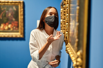 Woman visitor wearing an antivirus mask in the historical museum looking at pictures.