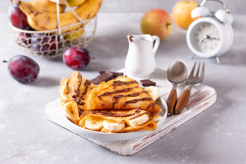 Crepes stuffed with chocolate spread and banana on white plate. Thin pancakes. Sweet dessert.
