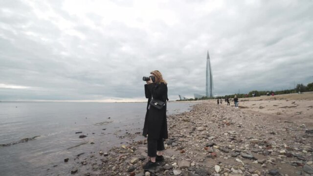 Woman takes photos on camera of sea in cloudy weather. Action. Professional photographer woman takes pictures of sea standing on background of cloudy sky