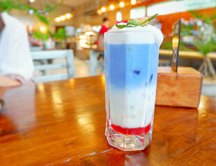 Fresh blue milk juice over coconut milk with ice in glass on wood table. The blue milk is popular menu for order. The taste is delicious. Close up.