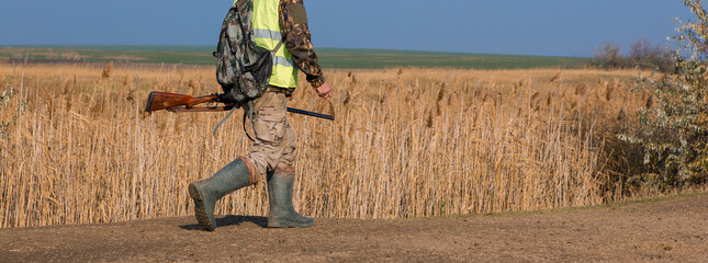 Hunter man in rural field with shotgun and backpack during hunting season