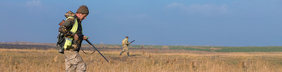 Hunters man in rural field with shotgun and backpack during hunting season