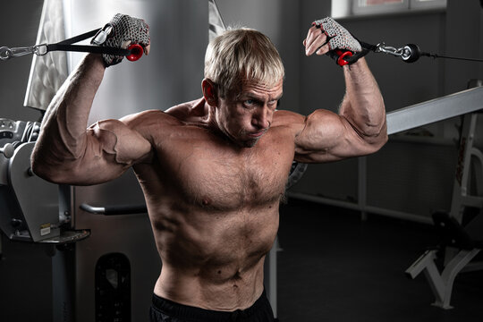 Muscular Adult Brutal Man Training On TRX Loops In The Gym. Portrait Of Caucasian Authentic Bodybuilder Doing Exercises In HIIT Workout