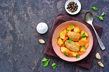 Hearty stew with potatoes, carrots and chicken meatballs in a pink bowl on a dark concrete background. Copyspace.