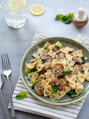 farfalle with mushrooms and spinach on a gray concrete background. vertical image