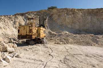 Fototapeta na wymiar A large yellow tracked excavator is mining rock in a quarry.