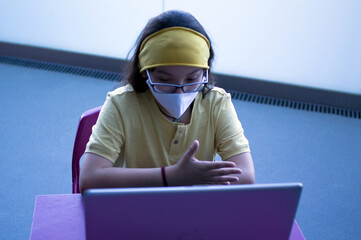 Teenager with a mask making video chat from the personal computer. A young man gestures while making a video conference, talking, studying or learning from his computer.