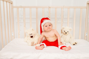 Obraz premium a small child is sitting in a crib in a Santa hat with stuffed toys bears, happy new year 2021, space for text
