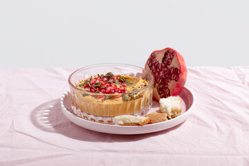 Pumpkin hummus dip with pomegranate and seed topping on pink textile background. Healthy Thanksgiving vegetarian appetizer. Copy space
