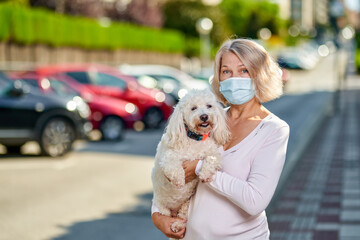 Woman an antivirus mask with a dog in her arms on a city street