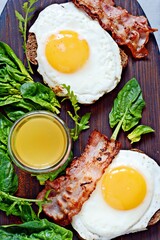 Breakfast fried eggs with bacon, fresh spinach, arugula and orange juice.
