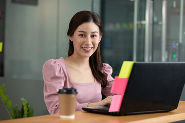 Happy Asian business woman in casual working with laptop and smile looking at camera at modern office or Co-Working Space,Business Startup Concept