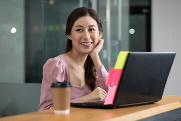 Happy Asian business woman in casual working with laptop and smile looking at camera at modern office or Co-Working Space,Business Startup Concept