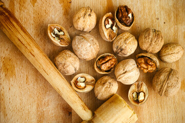 Walnuts and wooden kitchen hammer on wooden background.