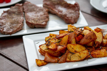 Grill dinner table. Roasted potato wedges with rosemary  and beefsteak on rectangular white plates