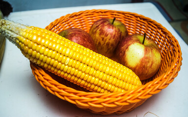 Raw sweet corn and apple arrange in a plastic wired bascket