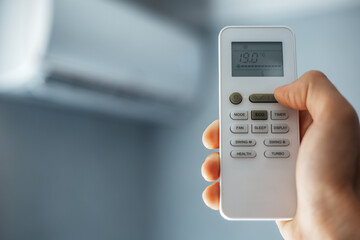 Close-up of male hand holding remote control of air conditioner.