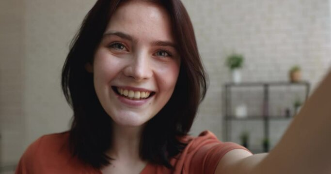 Beautiful lively 20s coquette woman holds smart phone recording video for social networks makes funny faces, dances moves flirting grimacing looking at camera, having fun alone at home, close up view