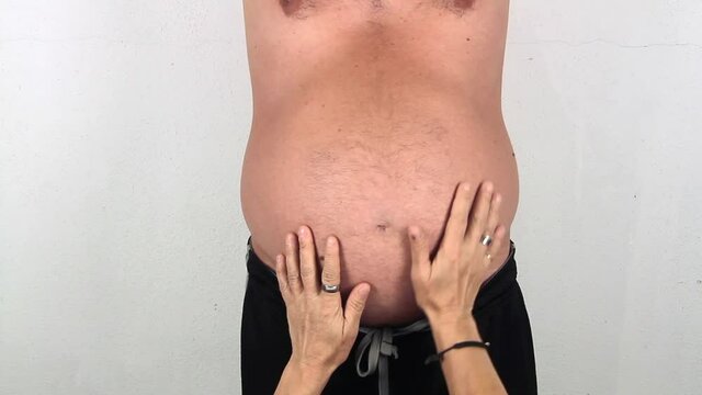 pot bellied man who is gently cuddled on the belly by the hands of his wife coming from below
