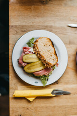 Top Down View of a Pastrami Sandwich with pickle and lettuce on a white plate with cutlery next to it