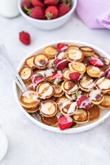 Obraz na płótnie Canvas Mini pancakes with strawberries on a light background. Tasty breakfast. Food trending. Baby food