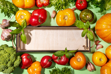 Top view harvest of fresh farm vegetables on pastel green background with mock up on empty small wooden box. Top view. Flat lay arrangement of vegetable harvest. Advertising healthy natural food.