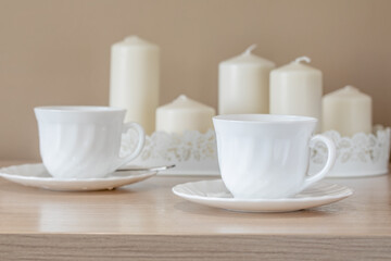 Fototapeta na wymiar two white cups and saucers on the background of a set of candles soft focus still life in high key