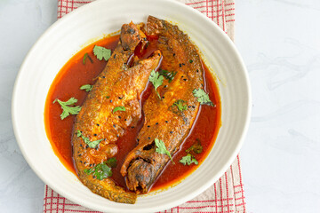 Spicy Indian Fish Curry in a Serving Bowl with Spoons Directly Above Horizontal Photo
