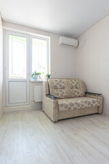 The interior of the room - a sofa, air conditioning and access to a balcony with plastic windows and a door