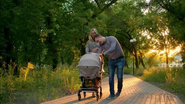 A caring father corrects a child lying in a stroller for a walk with his wife in the Park. A young couple walks in the Park with a baby stroller, the father adjusts the baby's pacifier